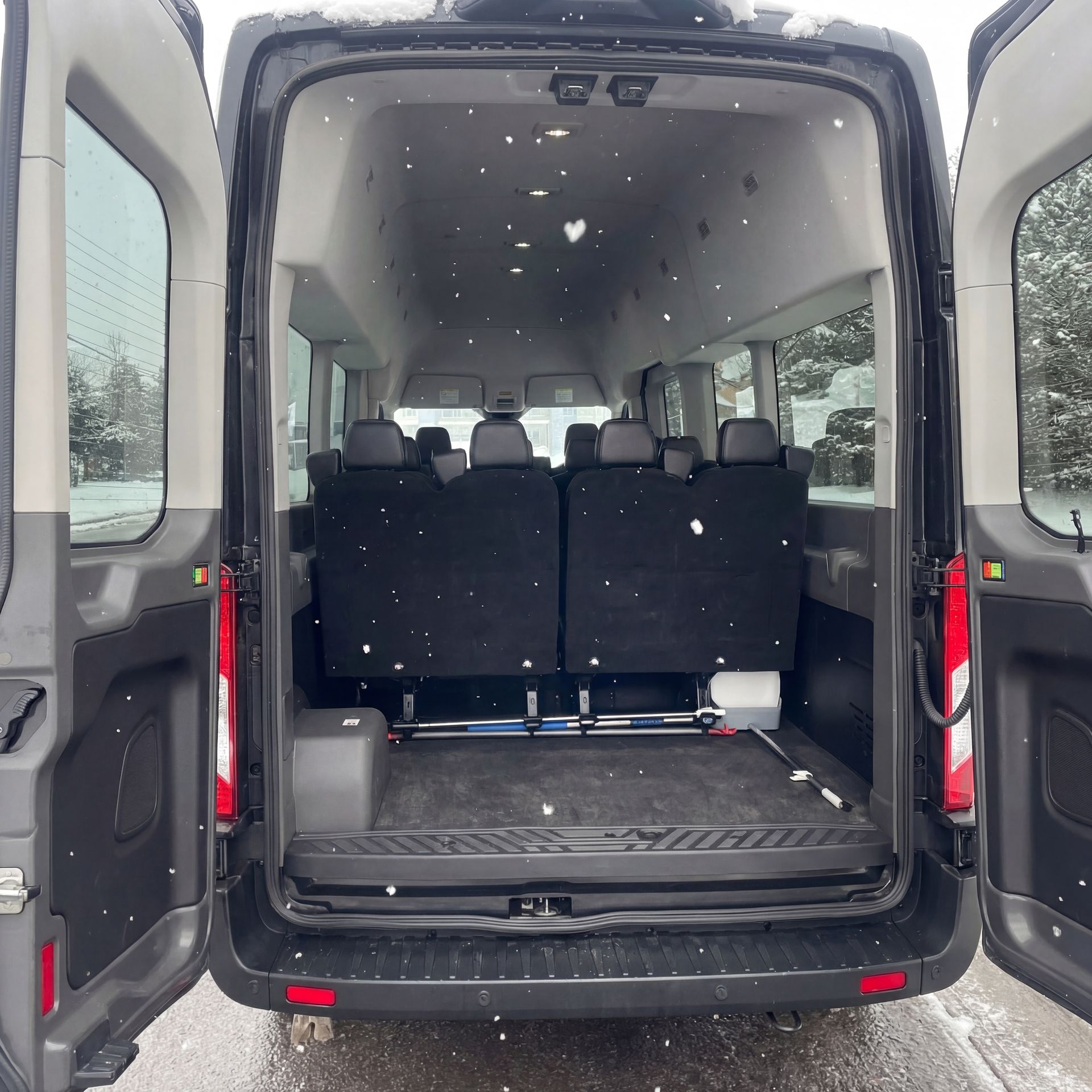 Back of a black passenger van, doors open, showing rows of seats and snowy outdoor setting.