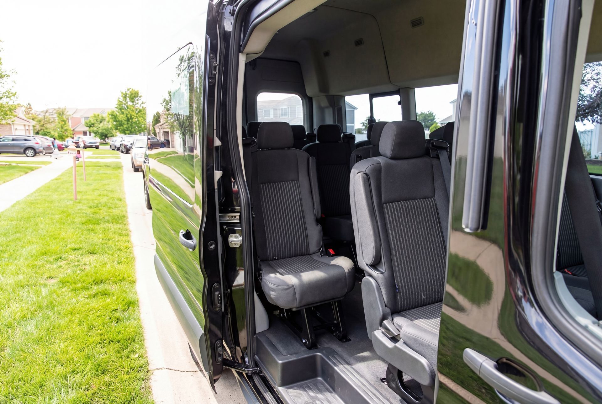 Black passenger van interior, seats visible through open sliding door, parked on a grassy verge.