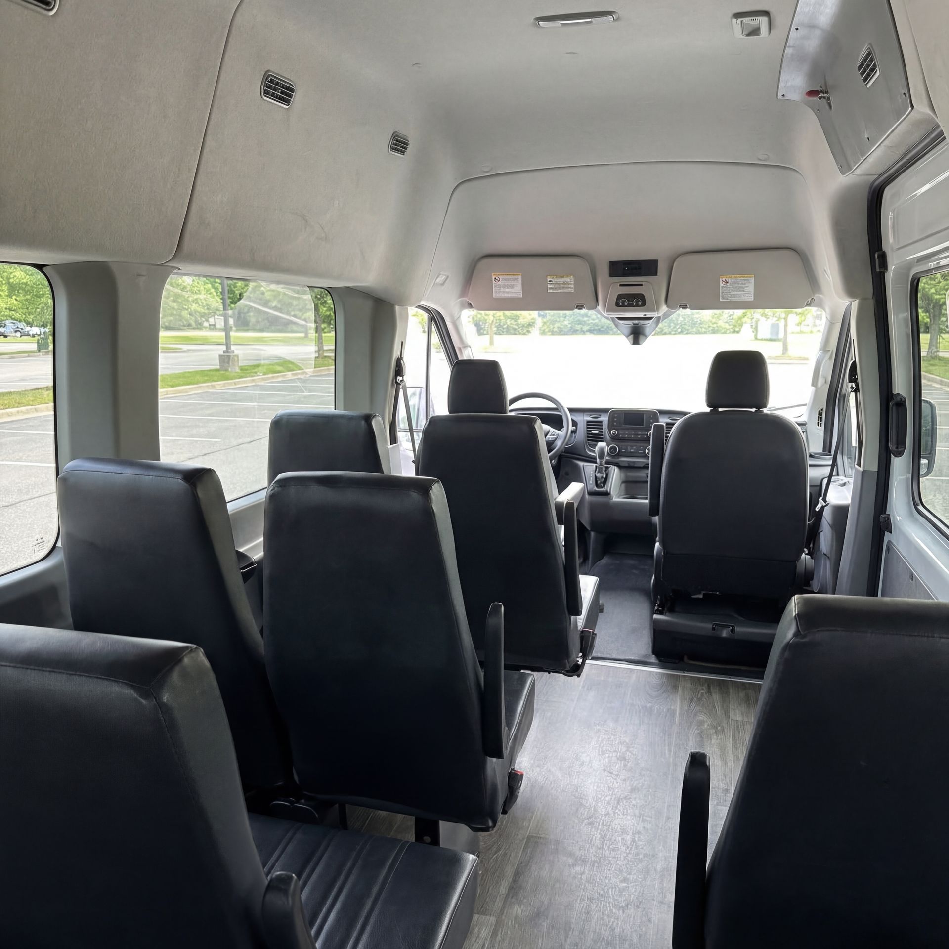 Interior of a passenger van with rows of black seats and a view towards the driver's area.