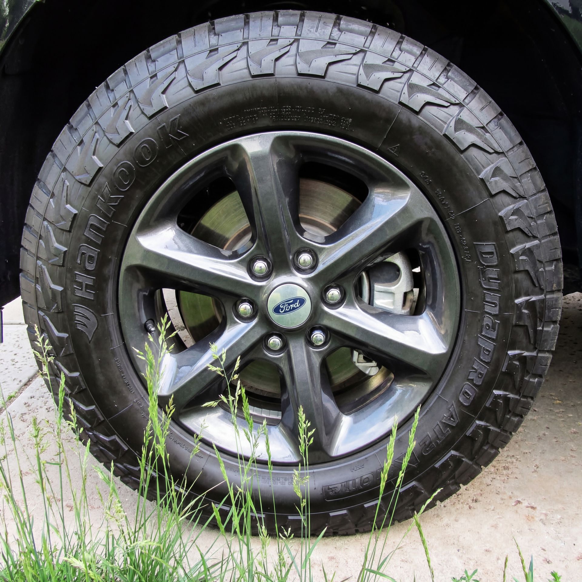 Gray alloy wheel with a Hankook Dynapro AT2 tire on a black vehicle.