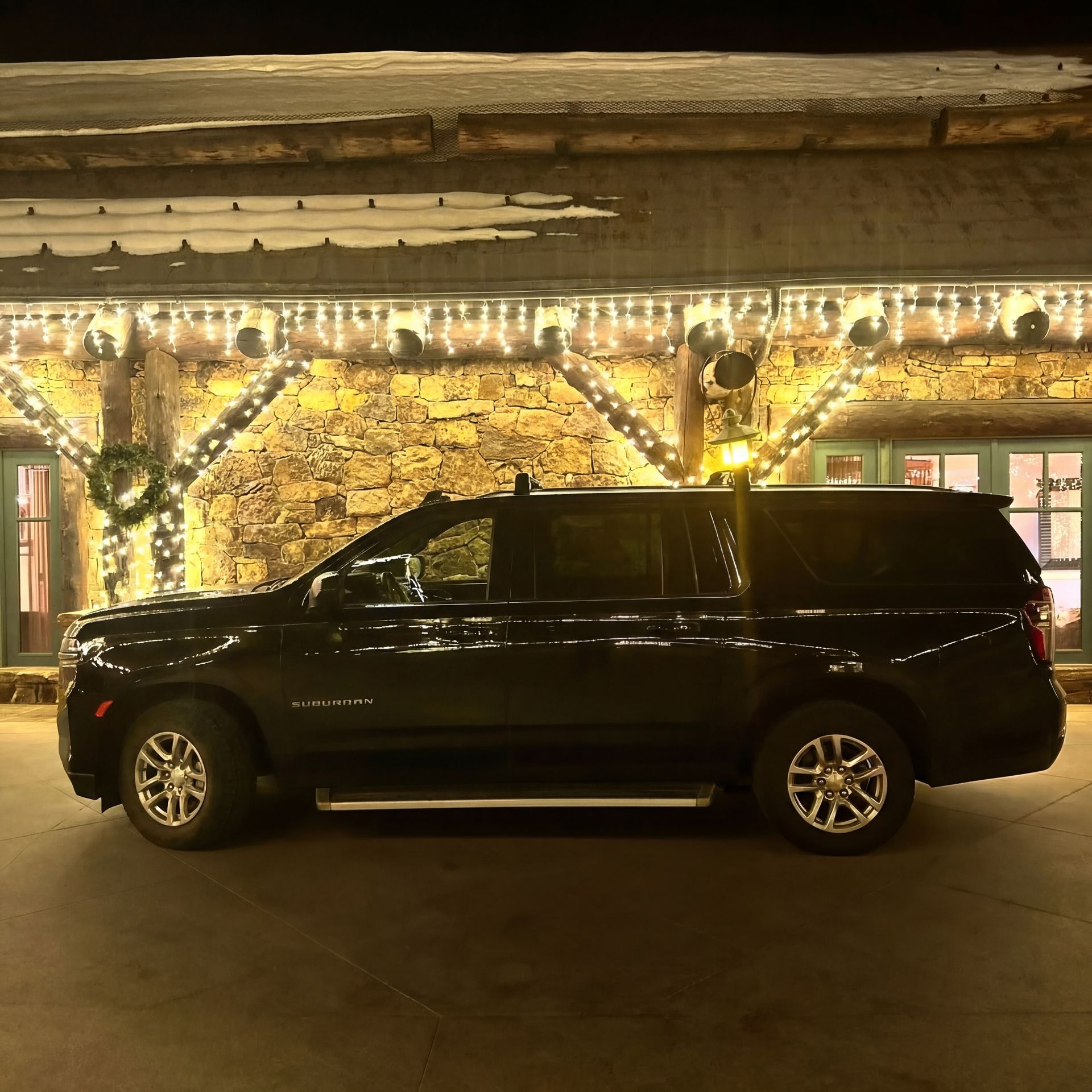 Black SUV parked in front of a stone building with holiday lights at night.