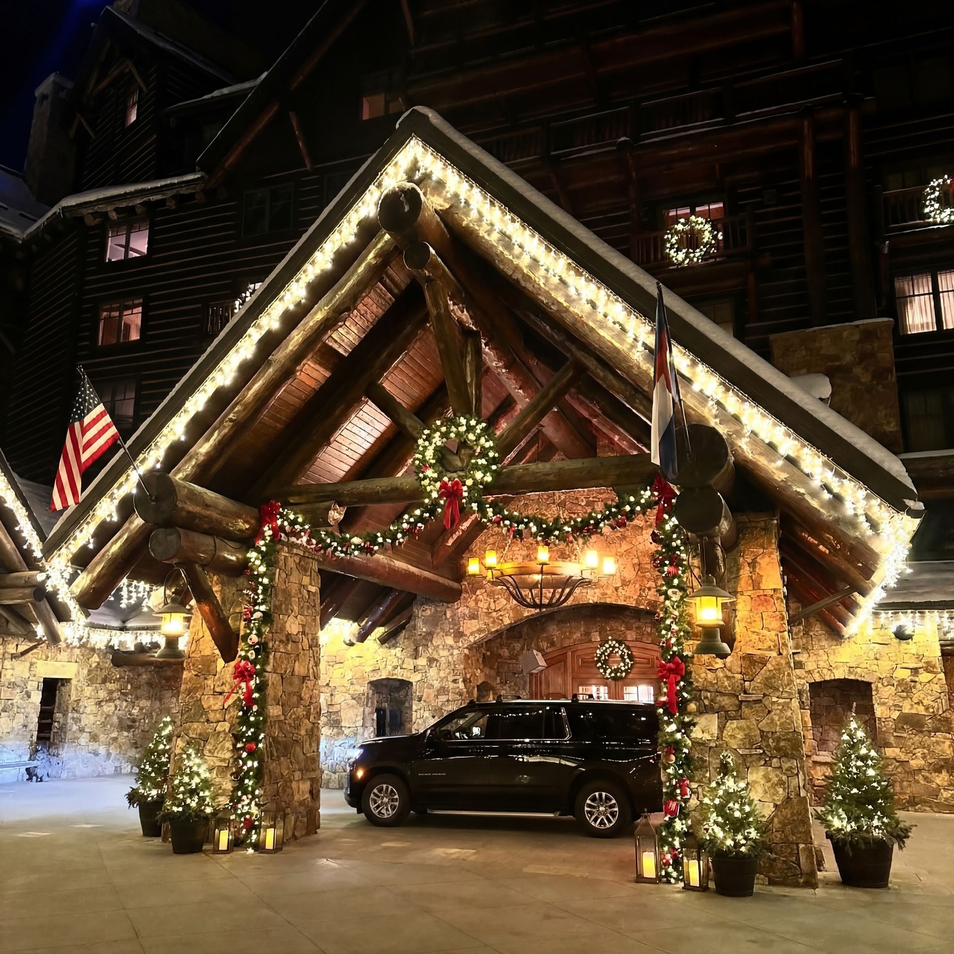 Lodge entrance decorated for Christmas; a black SUV sits under the portico. String lights, garland, and wreaths adorn the building.
