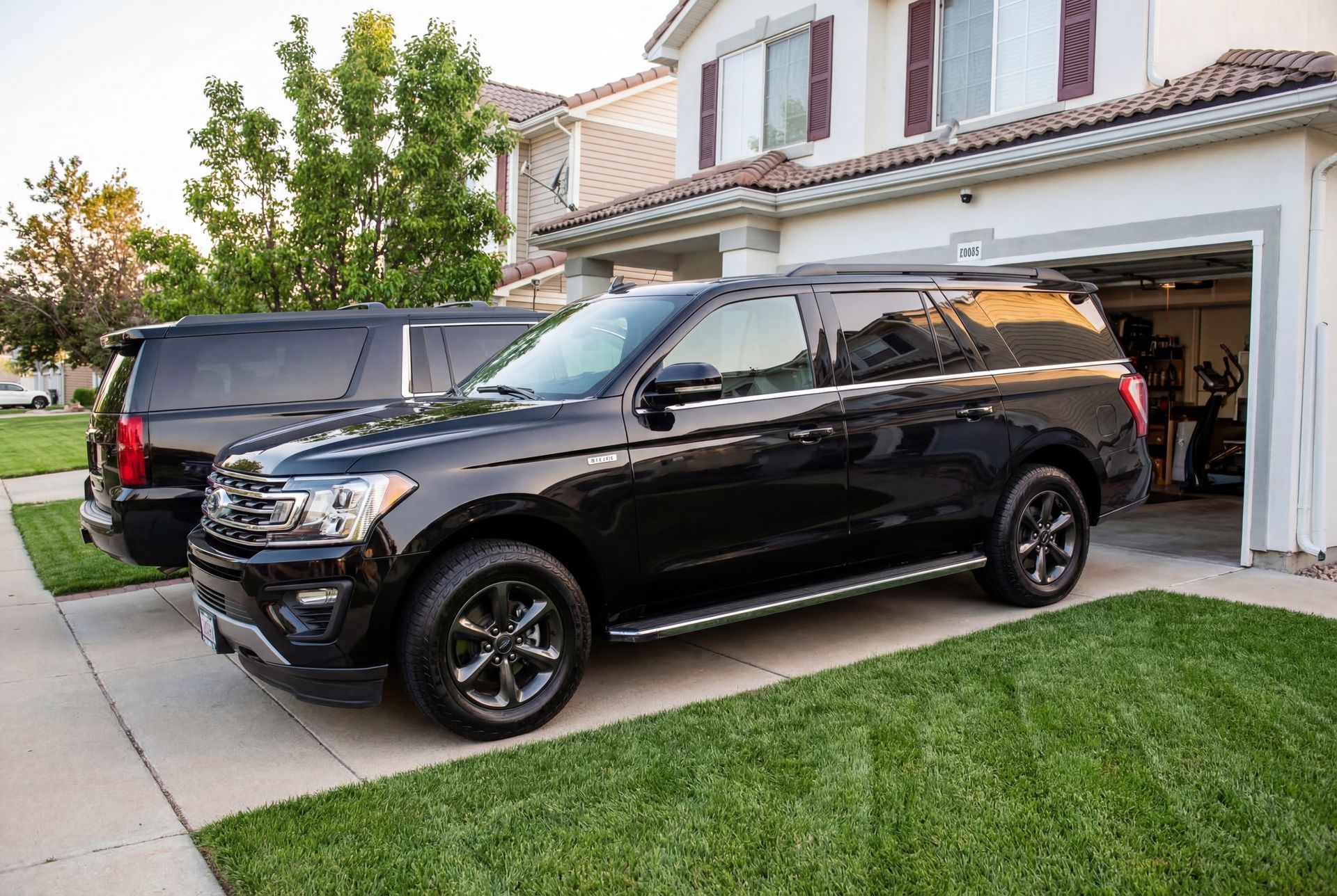 Black SUVs parked on a driveway in front of a house with a garage and green lawn.
