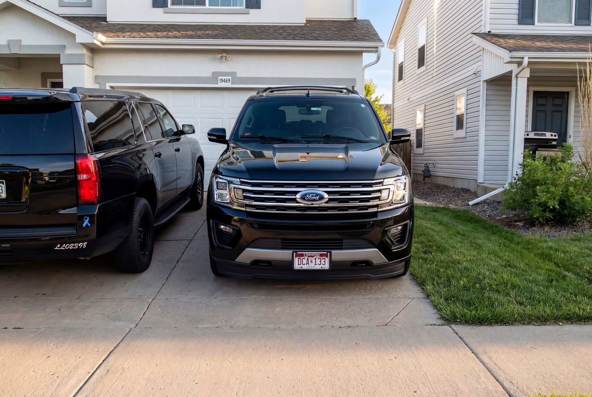 Two black SUVs parked in a driveway in front of a house.