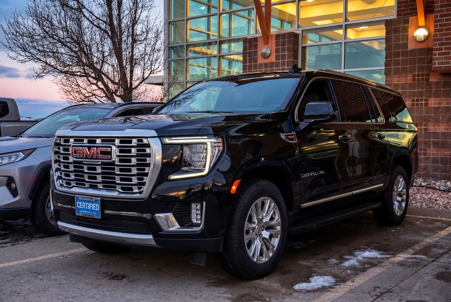 Black GMC Yukon Denali SUV parked in front of a building with glass windows; daytime.