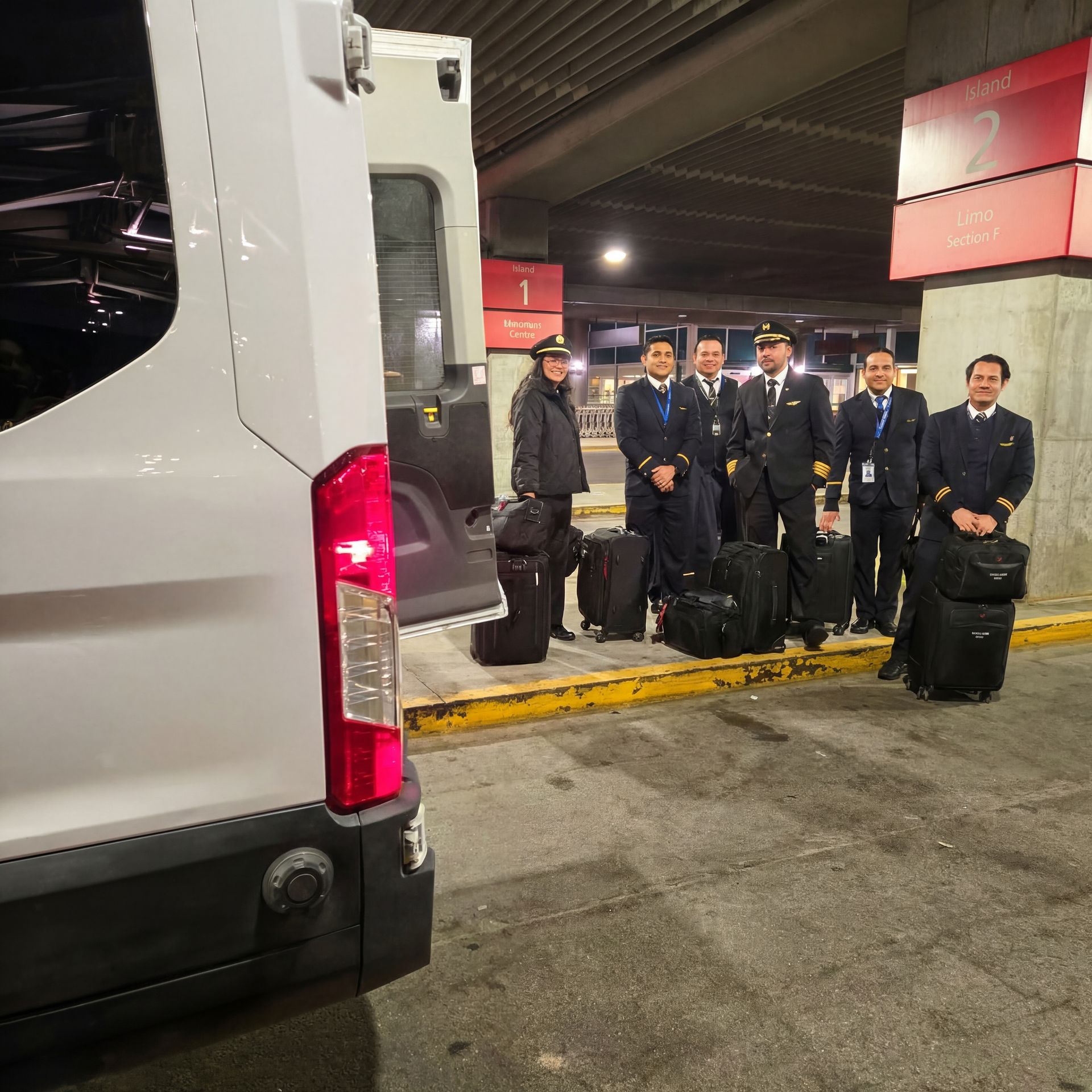 Pilots in uniform with luggage stand near a white van at a terminal.