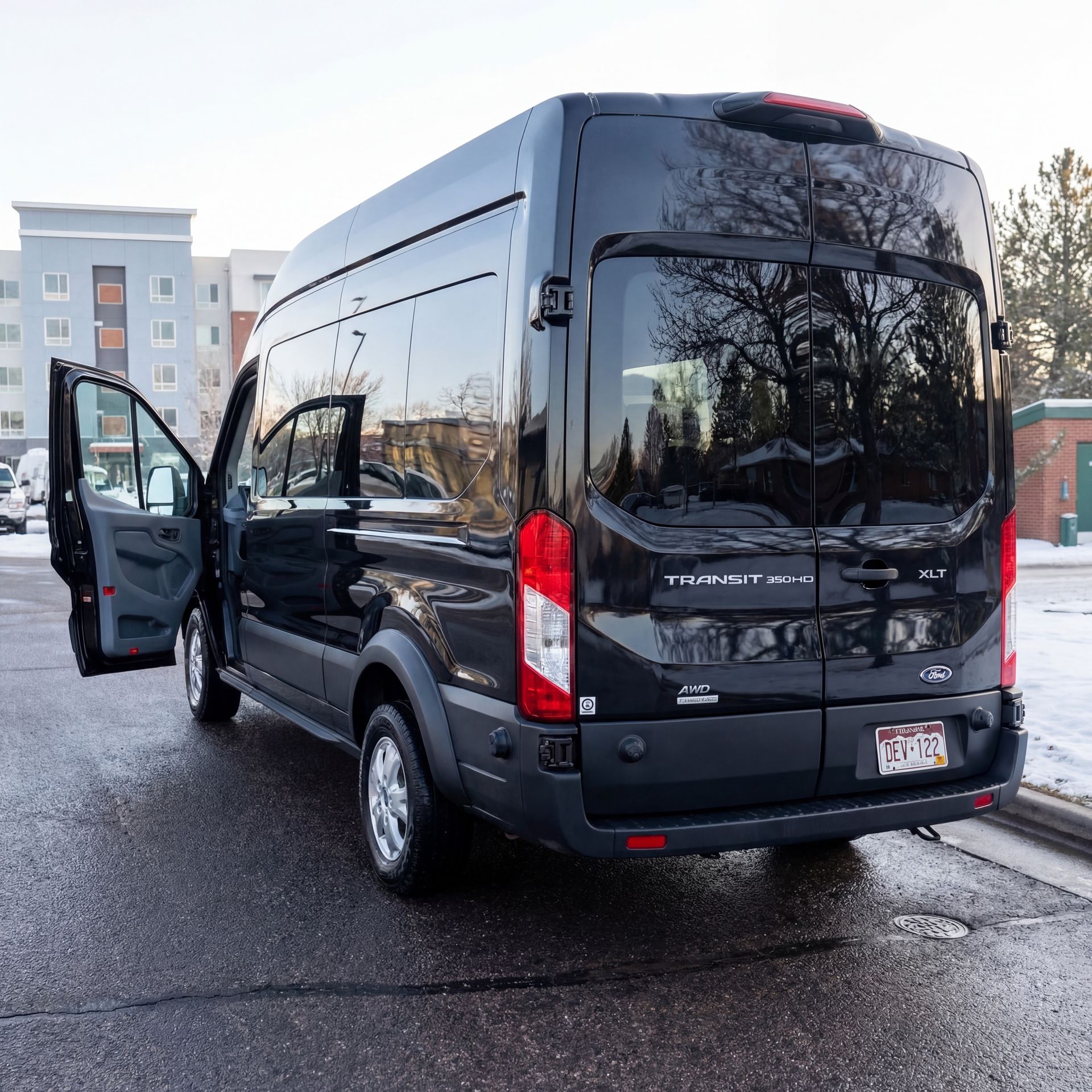 Black Ford Transit van parked with driver's side door open on a paved surface.
