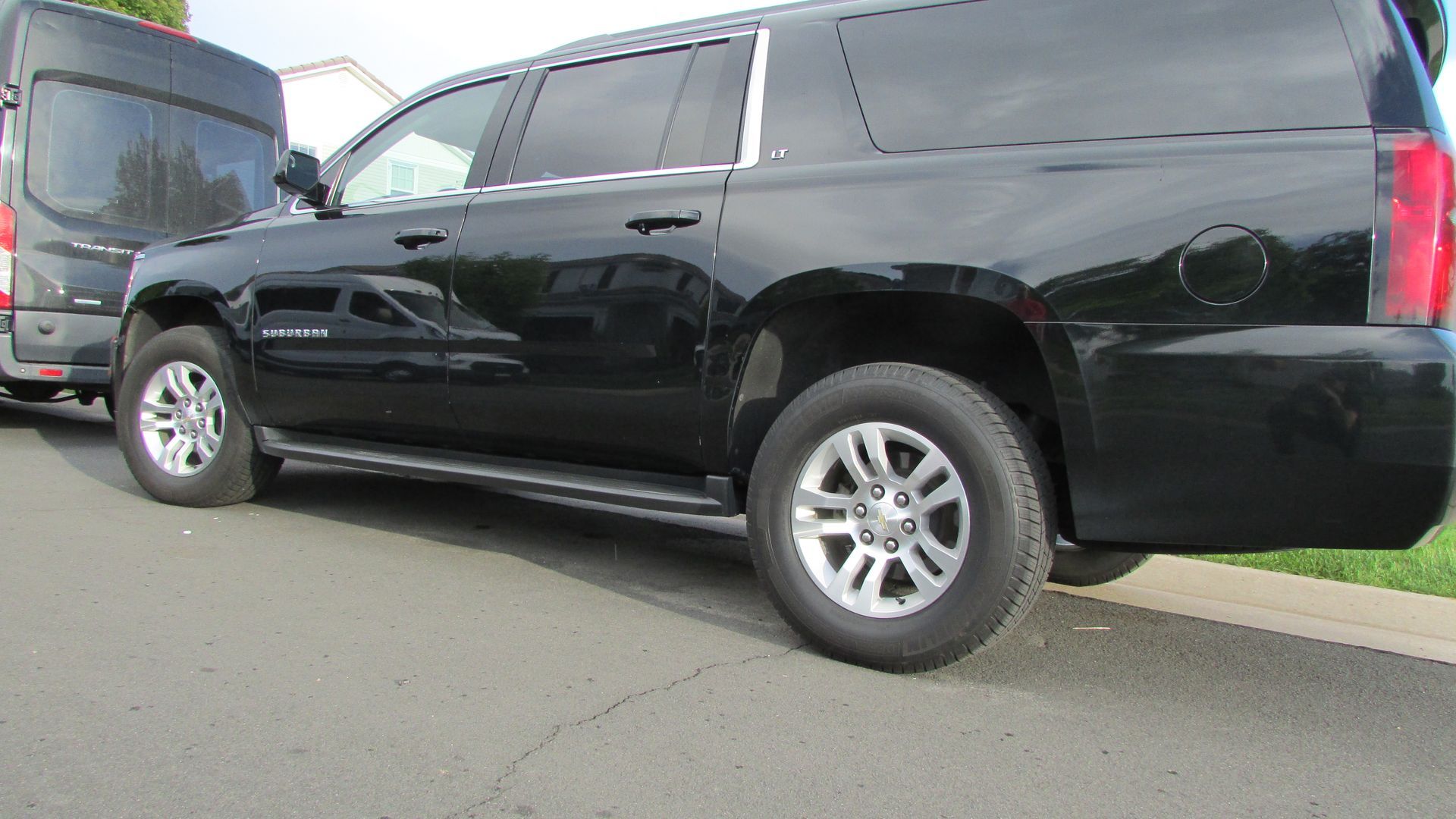 A black suv is parked on the side of the road next to a van.