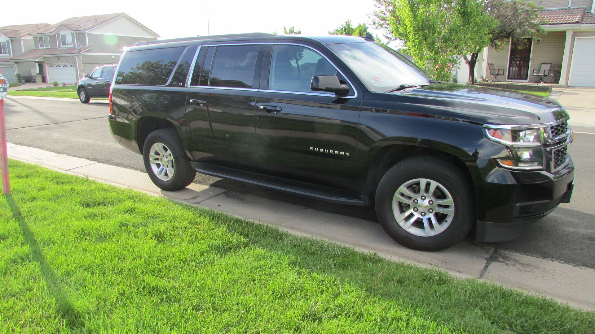 A black suv is parked on the side of the road in front of a house.