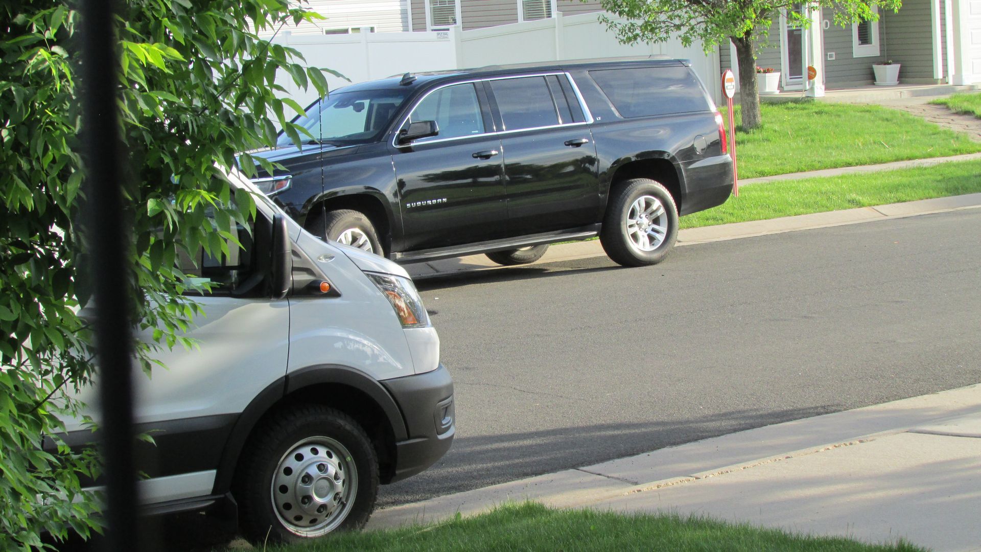 A black suv and a white van are parked on the side of the road