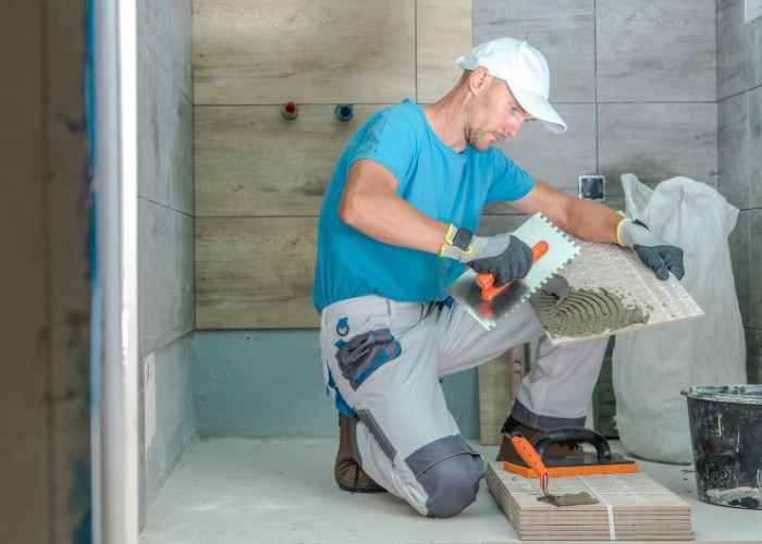 A man is installing a new wooden floor in a room with large windows, focusing on the details of the installation process.