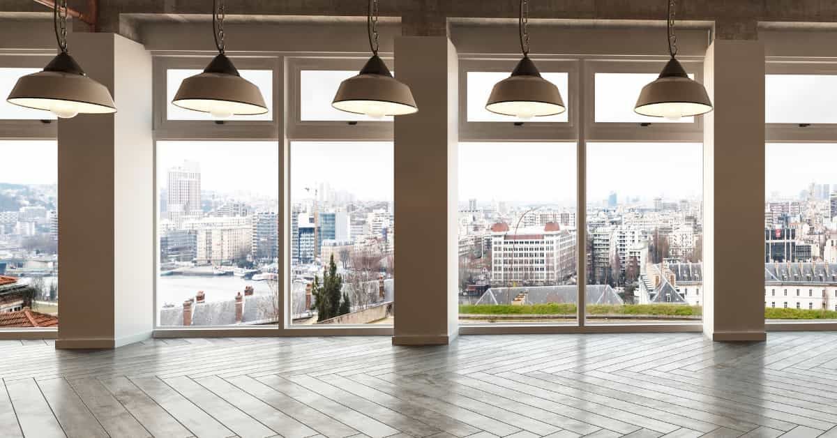 An interior room with large windows and beautiful flooring showcasing a city view is depicted