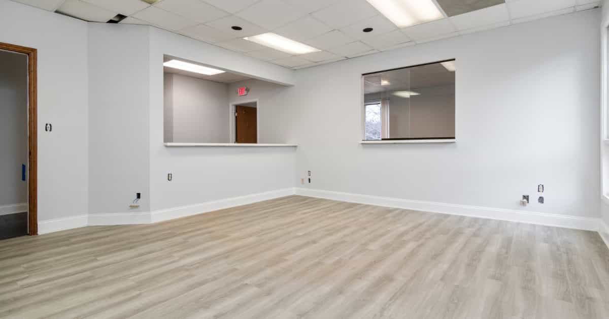 A brightly lit, modern office space with a light gray laminate floor and white walls.