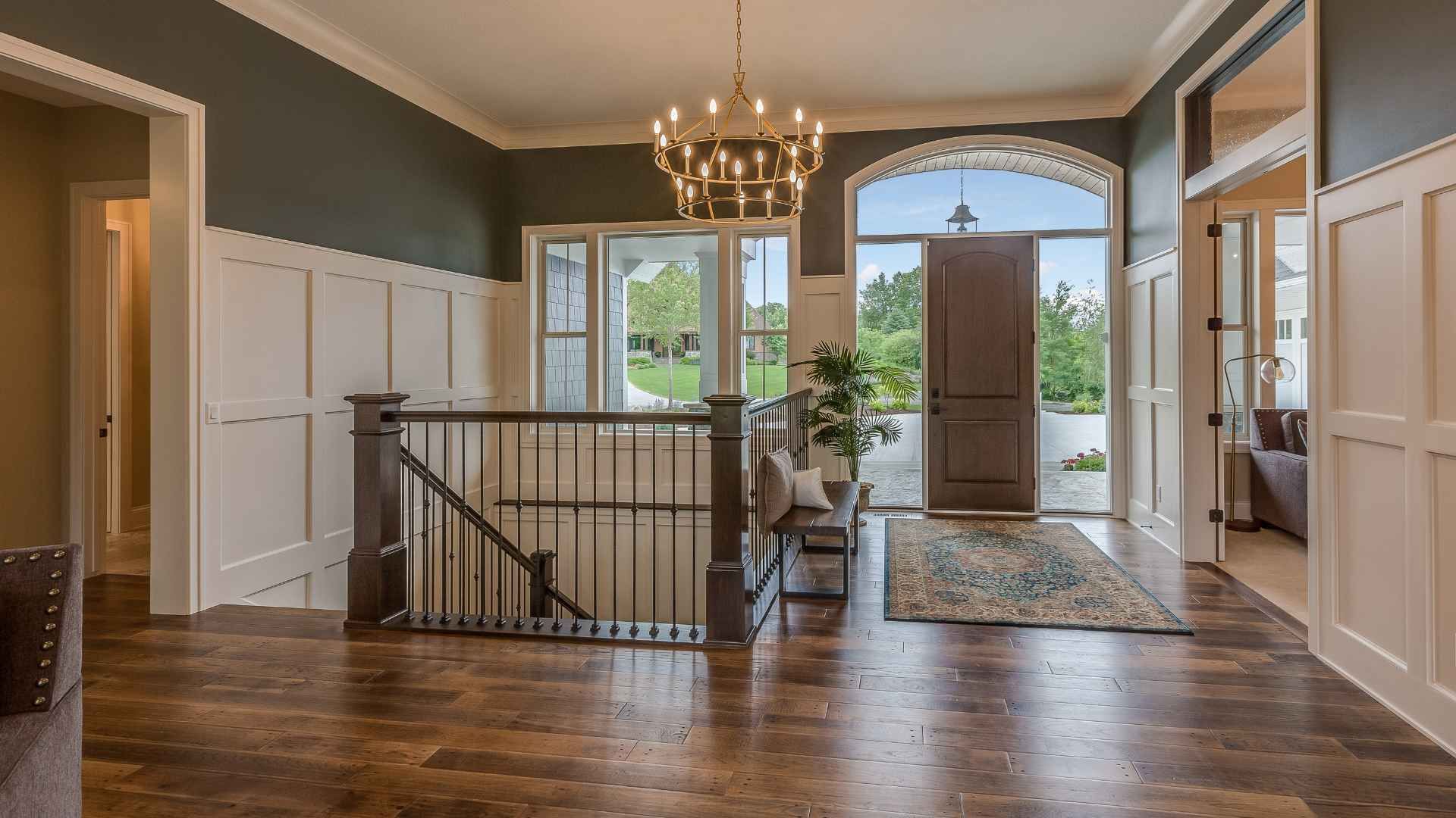 A spacious foyer with a large entryway, showcasing a luxury vinyl floor, a dark wooden door, and a chandelier.