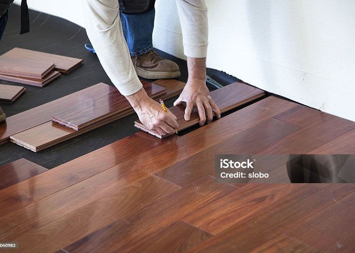 A person is measuring a piece of wood on a hardwood floor.