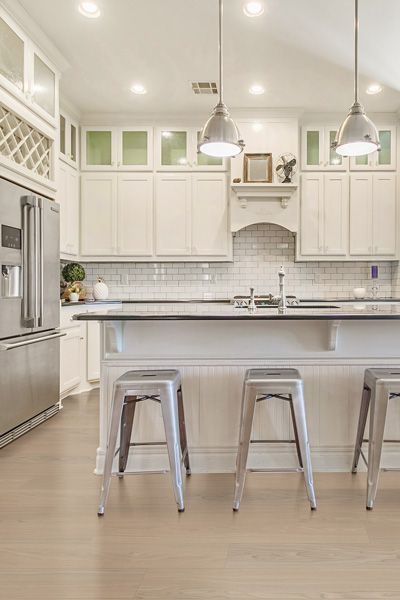 A kitchen with white cabinets , stainless steel appliances , a large island and stools.