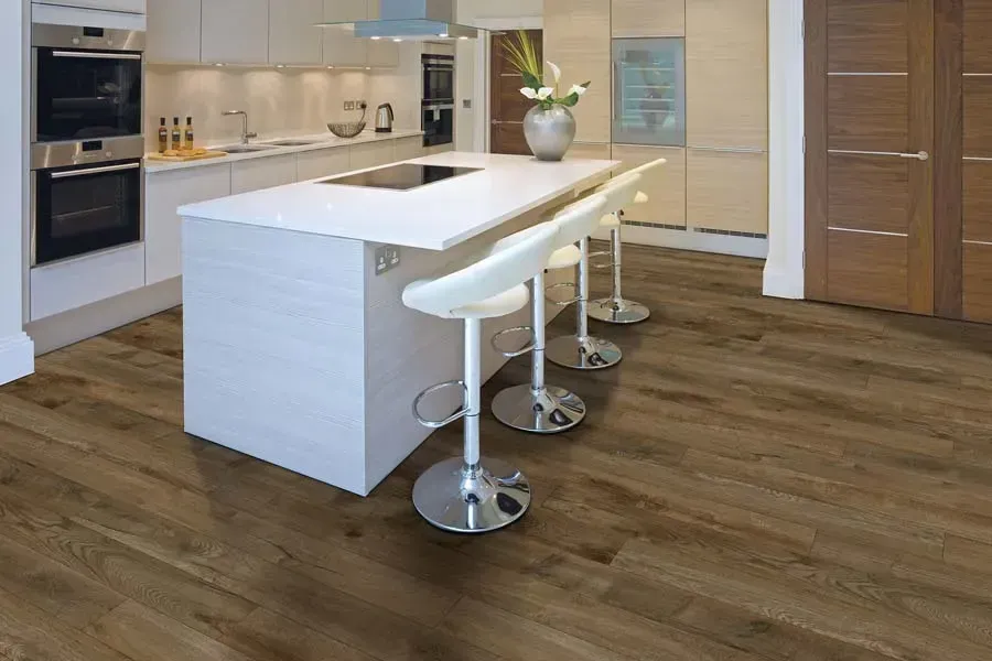 A kitchen with a large island and stools and a wooden floor.