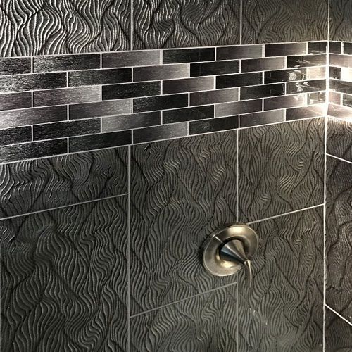 A close up of a shower with black tiles and a faucet.