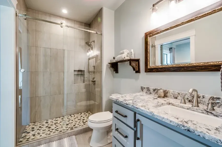 A bathroom with a toilet , sink , mirror and walk in shower.