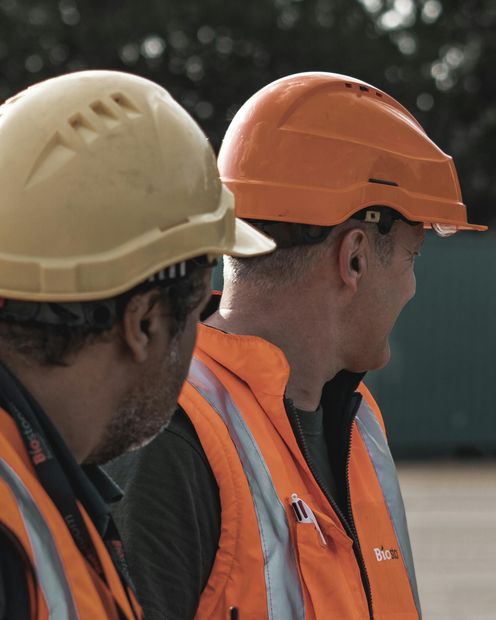 Two construction workers wearing orange vests and hard hats