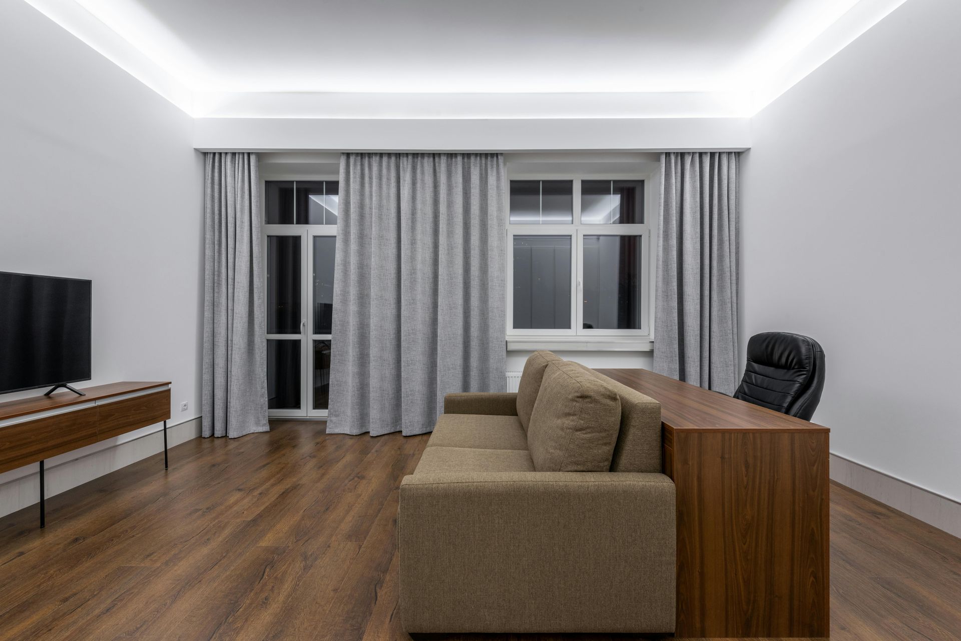 A living room with a couch , desk , television and curtains.