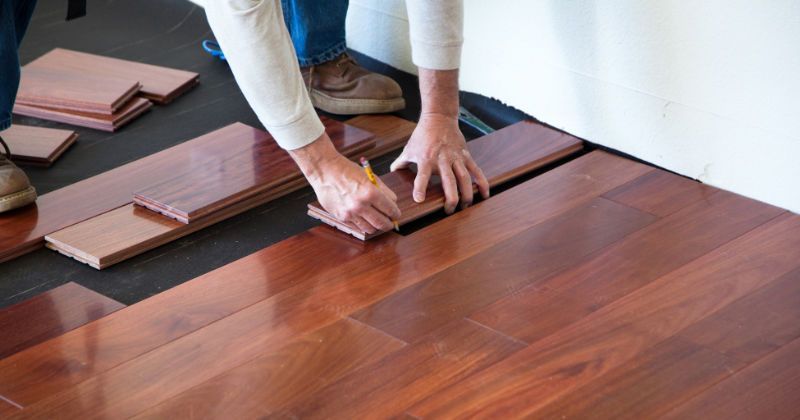 A person is measuring a piece of wood on a hardwood floor.