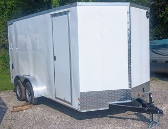 White enclosed cargo trailer with a black hitch parked on concrete.