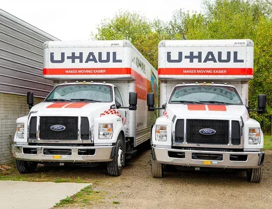 Two white U-Haul trucks parked next to a building. Red and orange accents, sunny day.