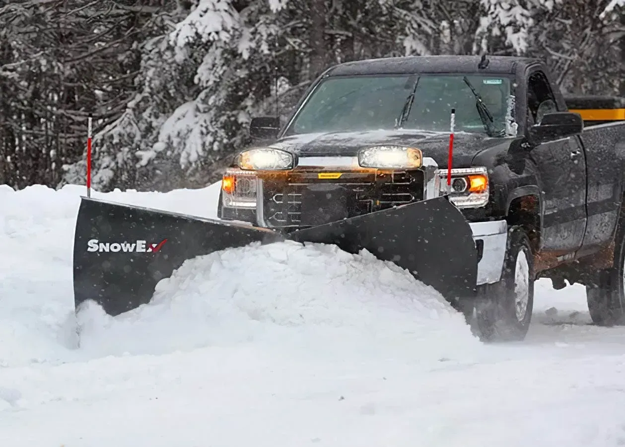 Black pickup truck plowing snow with a snowplow in a snowy environment.