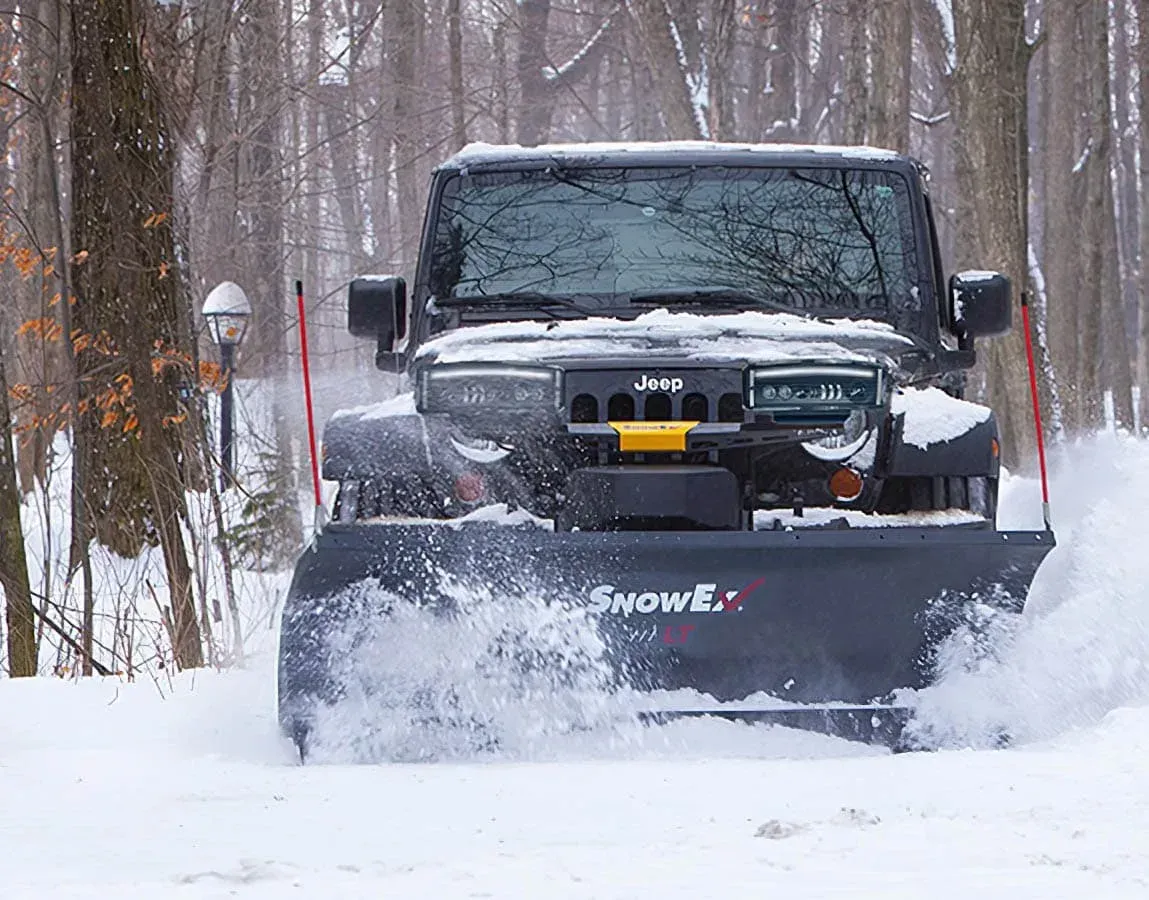 Black Jeep plowing snow on a snowy road, trees in the background.