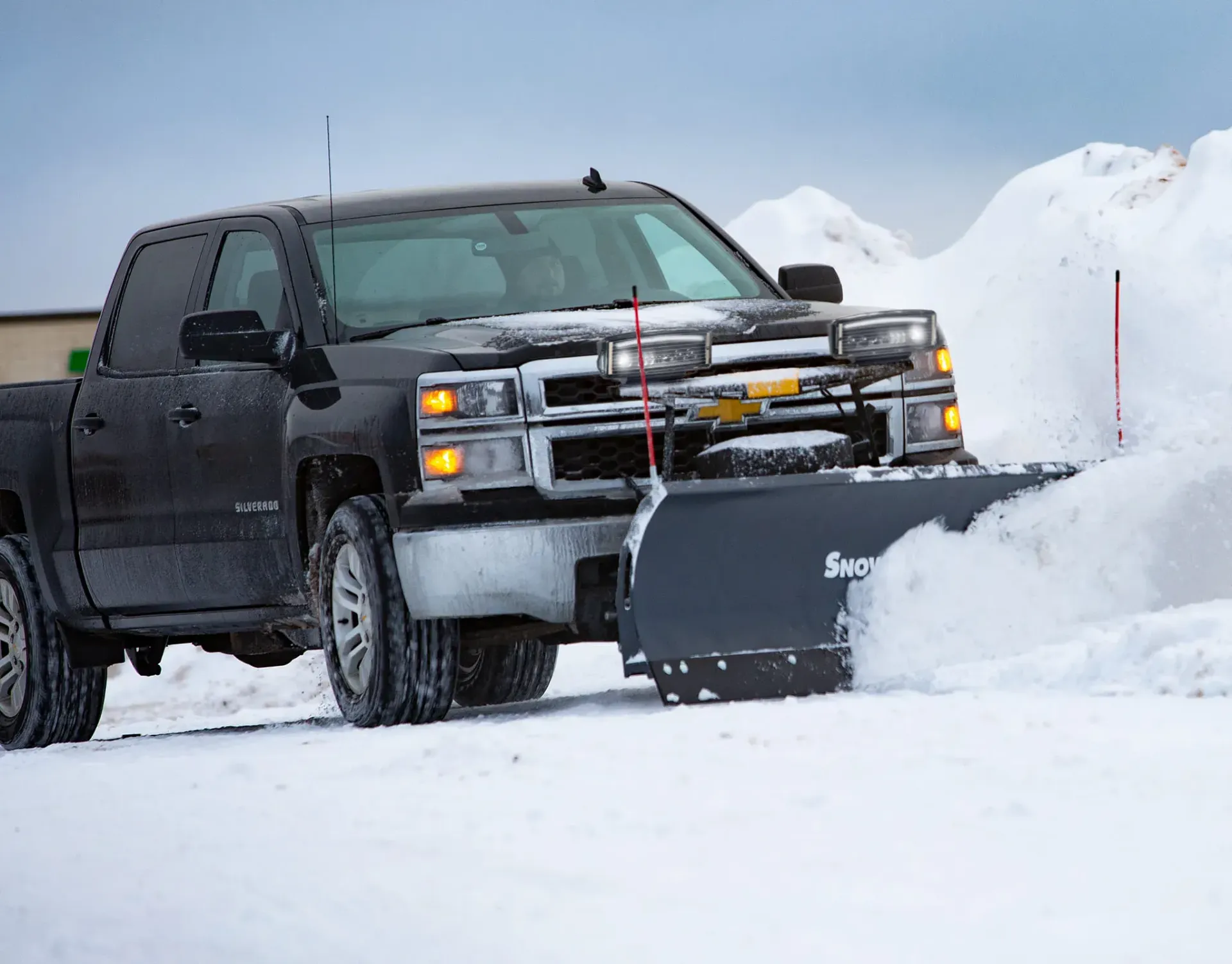 Black pickup truck plowing snow, with a snow-covered setting and low visibility.