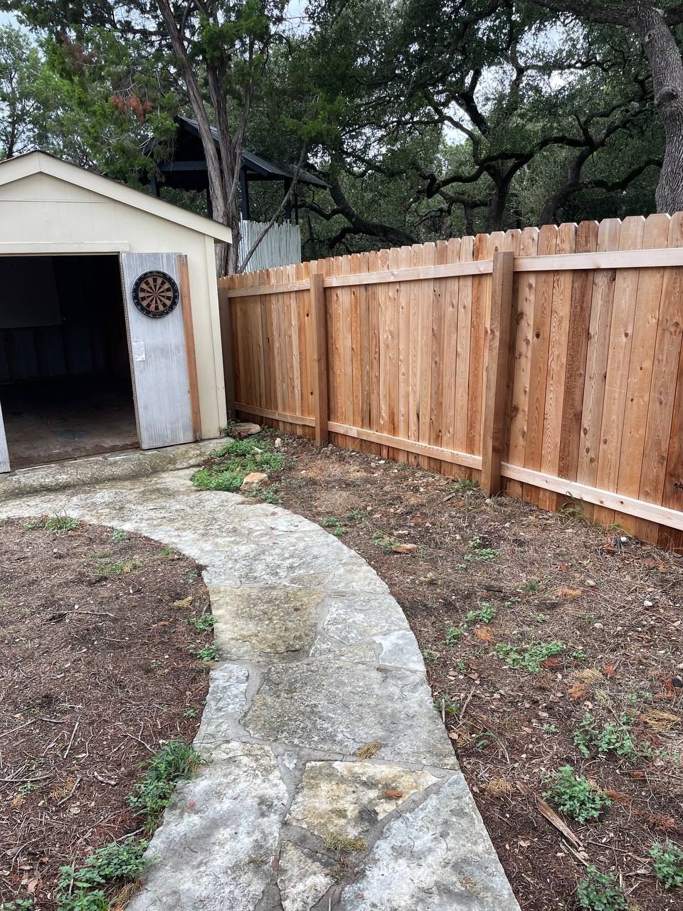 A wooden fence surrounds a shed in a backyard.