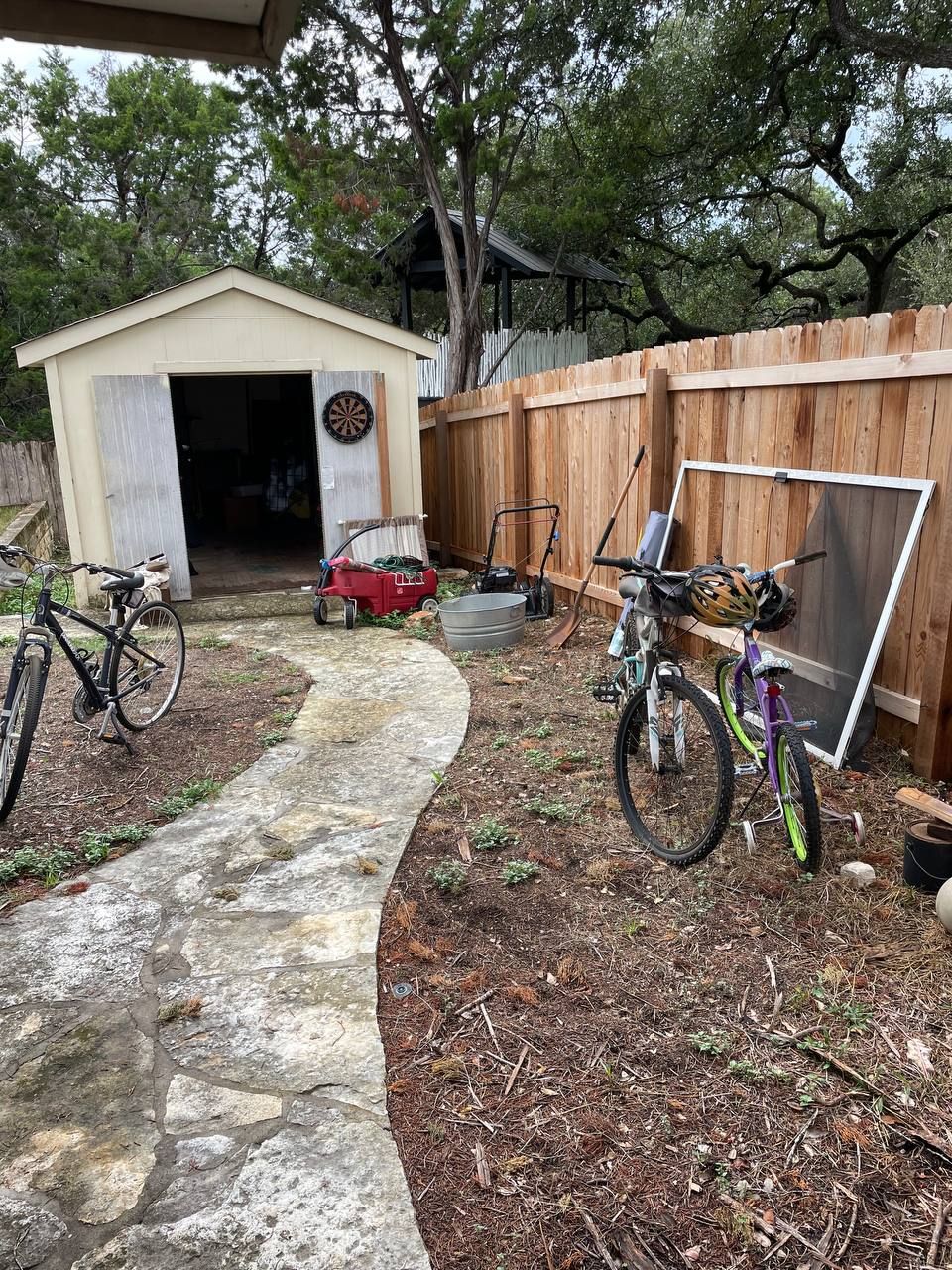 Two bicycles are parked in a backyard next to a wooden fence.