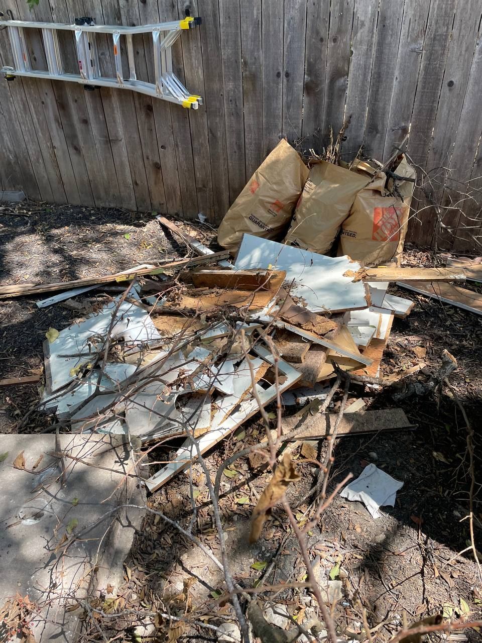 A pile of trash is sitting in the dirt in front of a wooden fence.