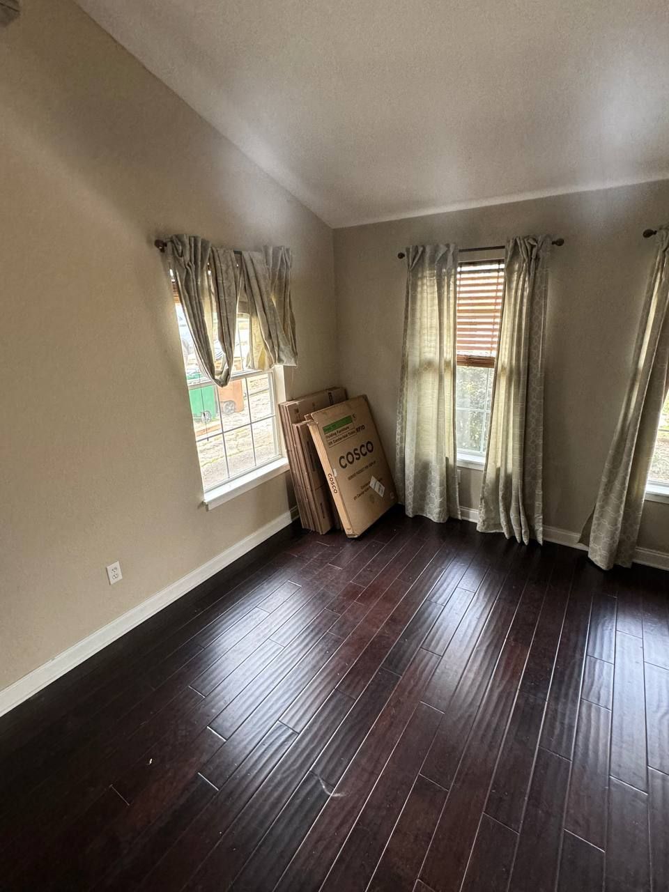 An empty room with hardwood floors and two windows.