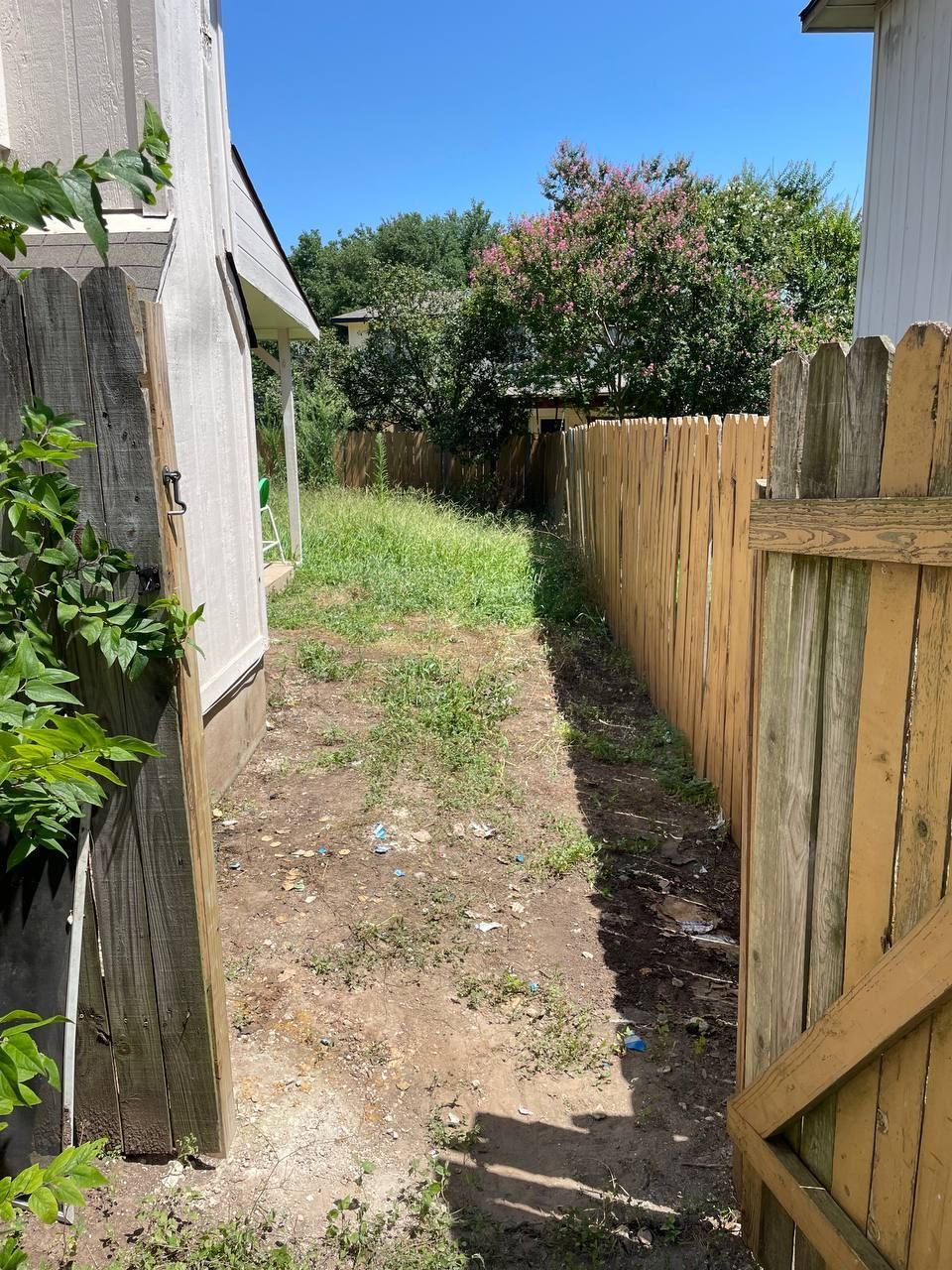 A wooden gate is open to a dirt path leading to a house.