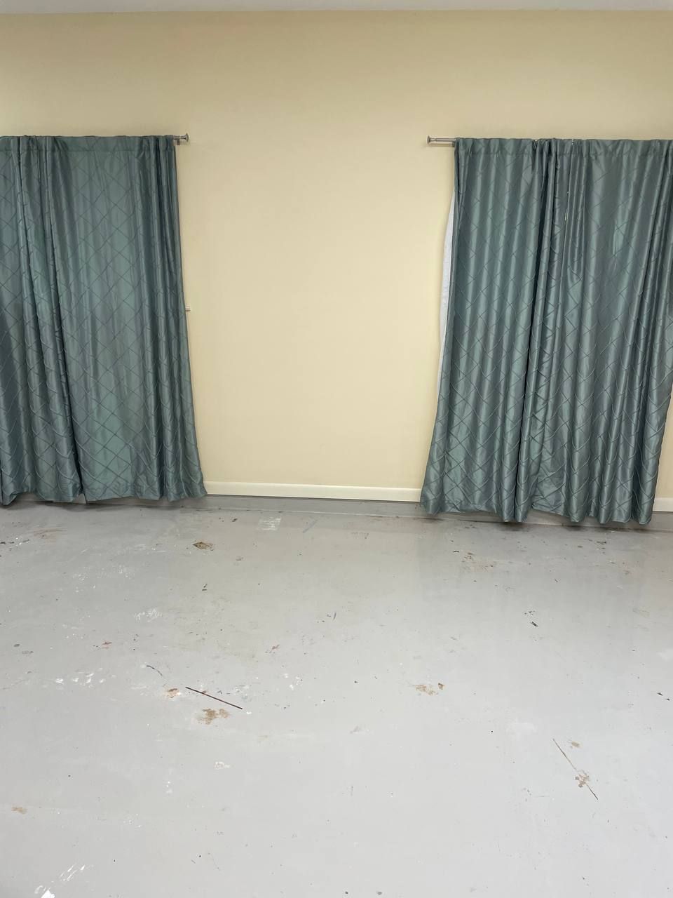 A room with two curtains on the windows and a gray floor.