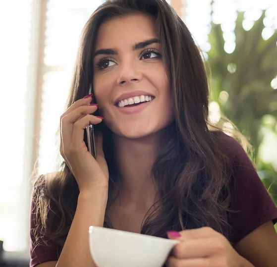 A woman is talking on a cell phone while holding a cup of coffee.