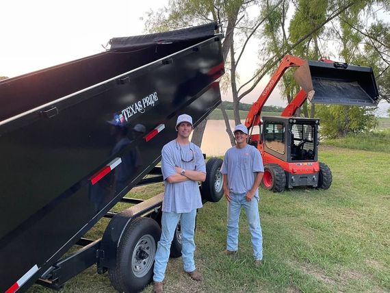 Two men are standing in front of a dumpster and a bulldozer.