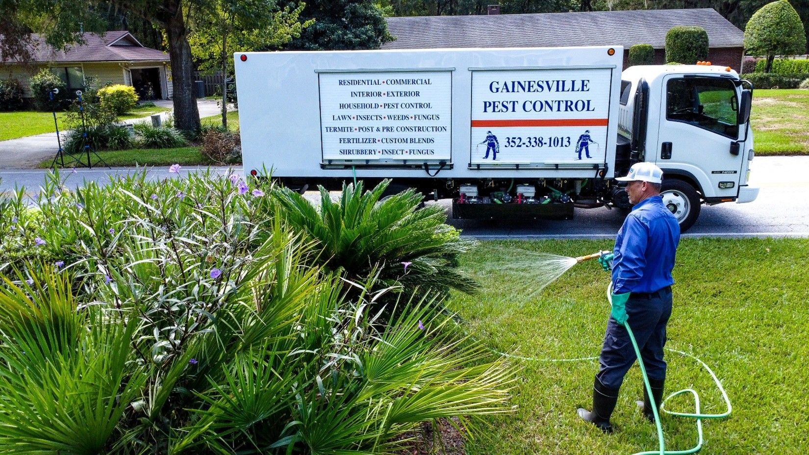Man sprays lawn with hose, pest control truck in the background.