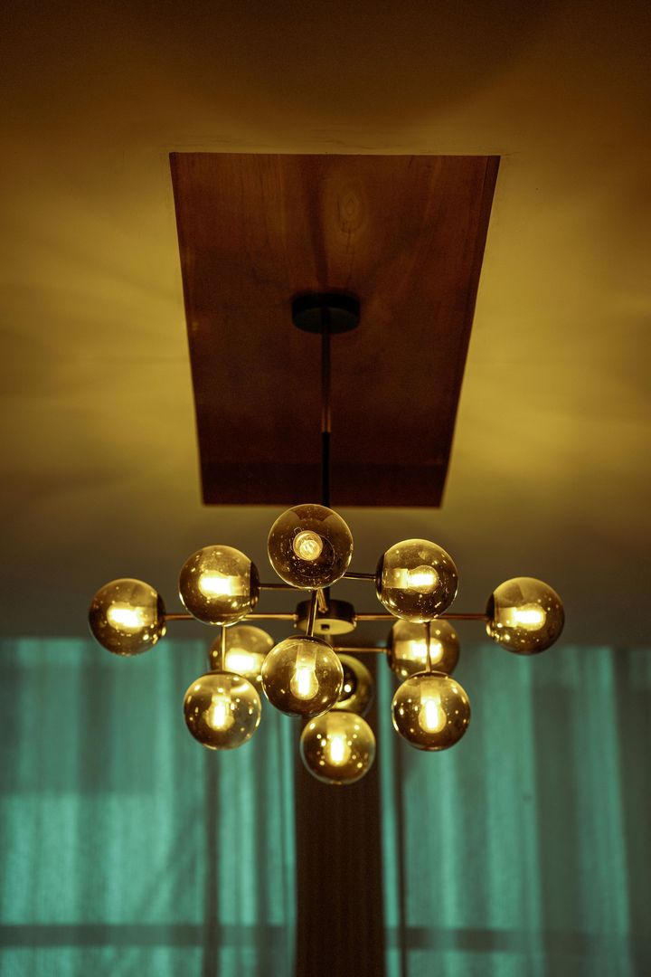 Brass chandelier hanging beneath a wooden ceiling panel above green curtains
