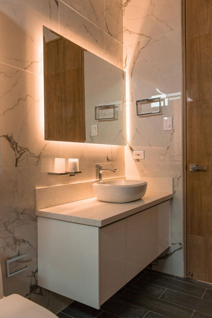 Modern bathroom vanity with round sink, backlit mirror, and wooden door.