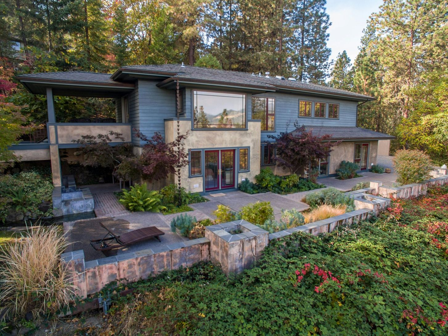 Modern two-story house with stone landscaping, large windows, and forested hillside setting