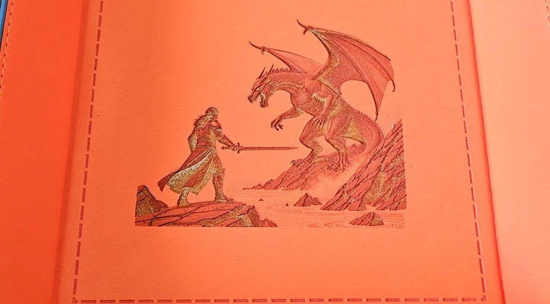 Red cover with a small stitched scene of a knight facing a dragon and a castle.