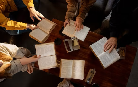 A group of people are sitting around a table reading books.