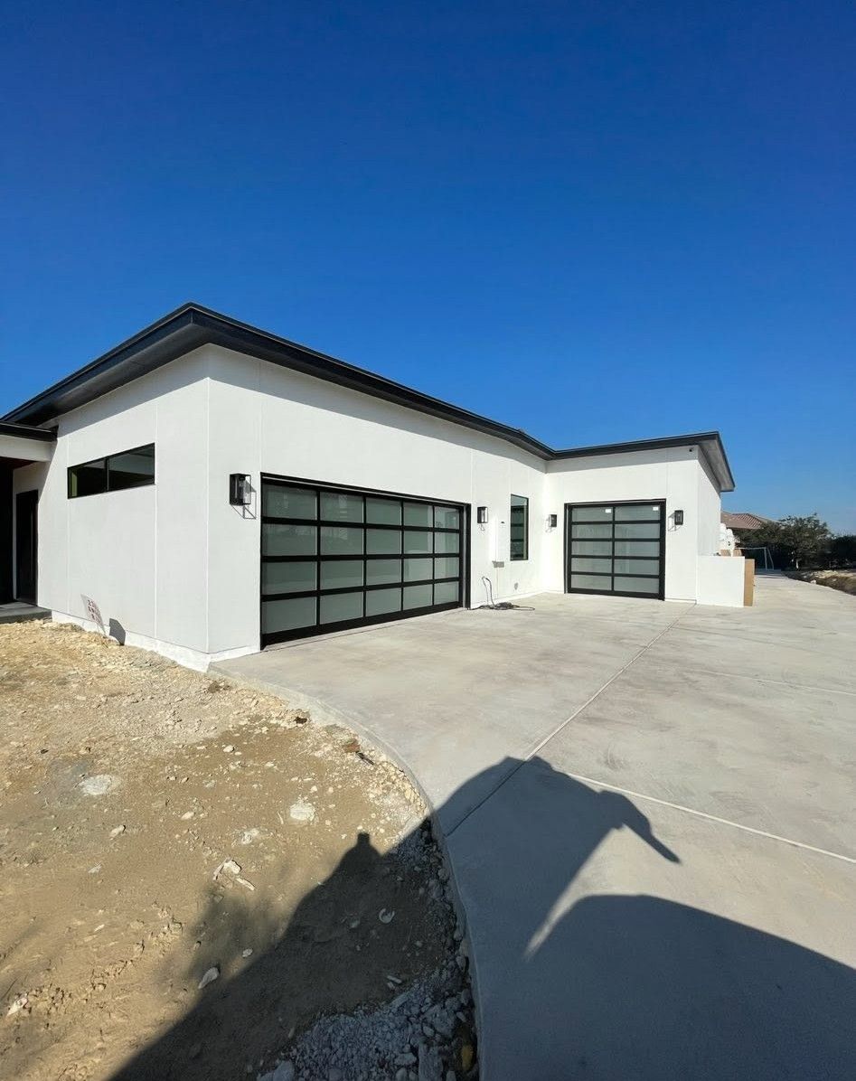 Modern white house exterior with black garage doors and a concrete driveway under a clear blue sky