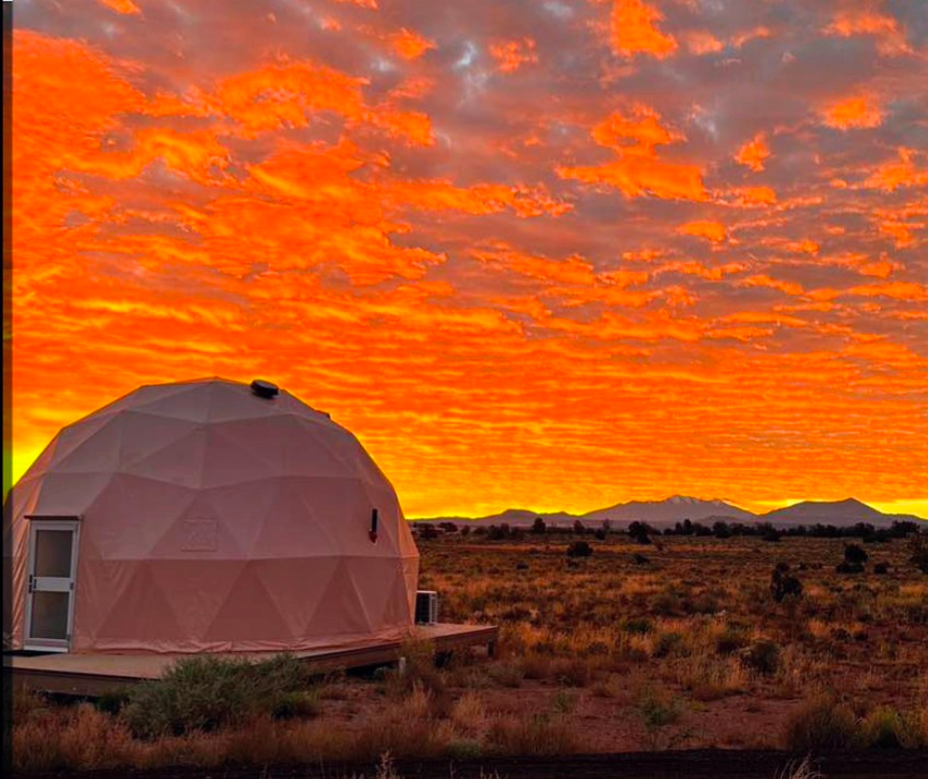 Geodesic dome cabin in a desert under a vivid orange sunset sky