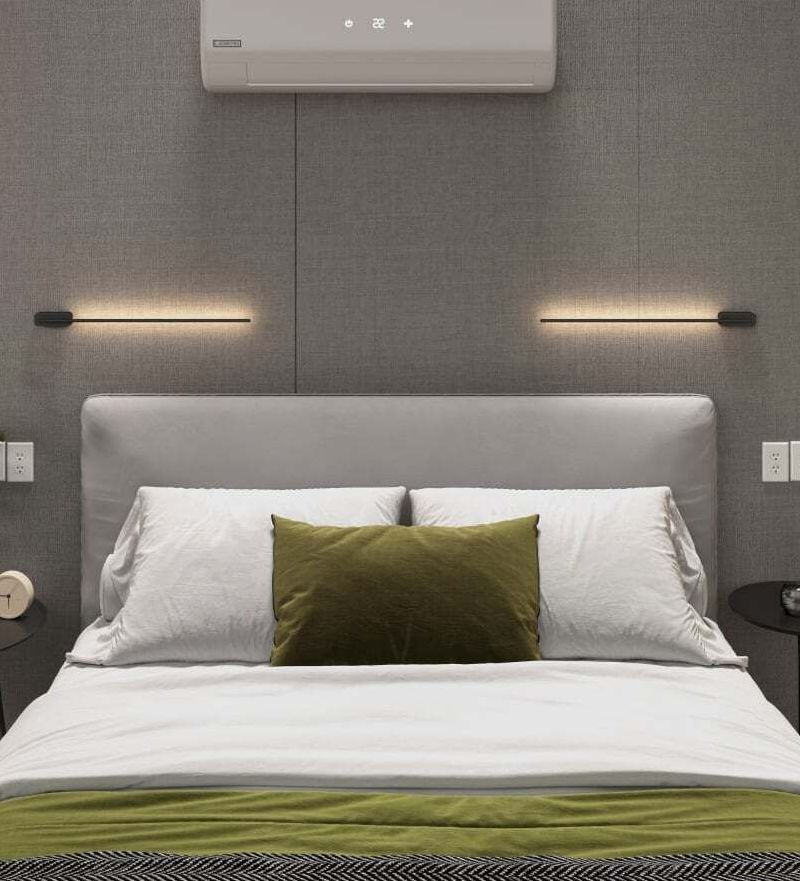 Modern bedroom with gray upholstered bed, white bedding, green accent pillow, and wall lights beneath an air conditioner