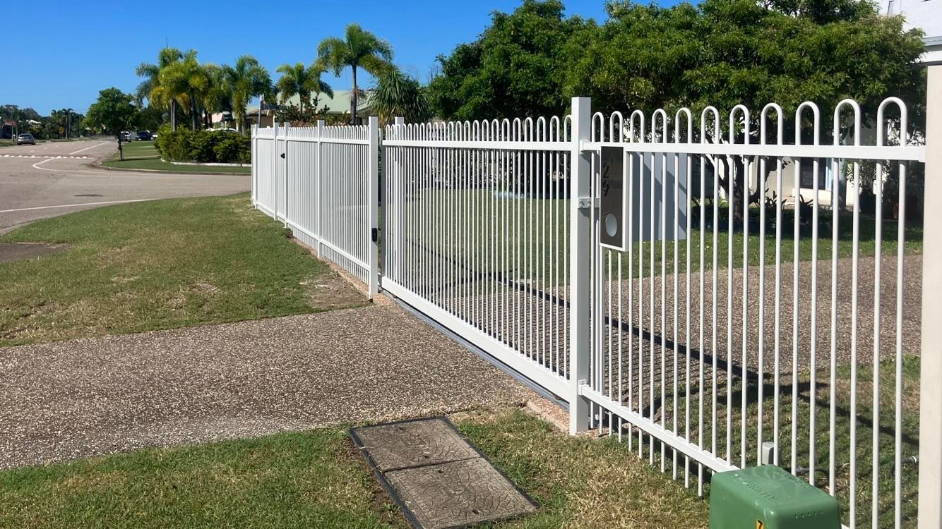 White metal fence with decorative top along a grassy area, a concrete path, and trees in the background — Gate-O-Matic in Garbutt, QLD