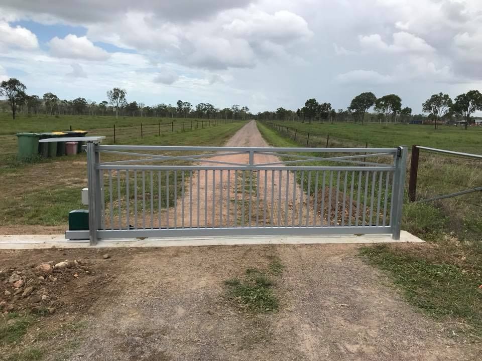 Metal Sliding Gate Across a Dirt Driveway Leading Into a Field, Under a Cloudy Sky — Gate-O-Matic in Garbutt, QLD